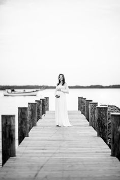 a pregnant woman standing on a dock in front of the water with her arms crossed