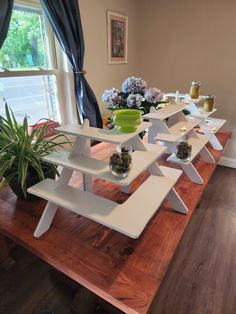 a wooden table topped with white shelves filled with vases and potted plants next to a window