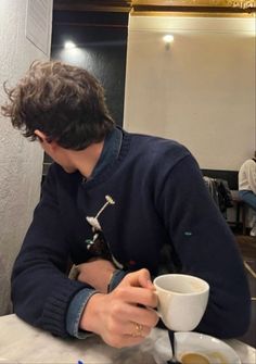 a young man sitting at a table with two cups of coffee in front of him