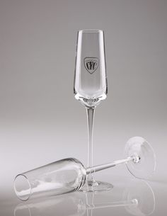 an empty wine glass next to a clear wine goblet on a reflective surface