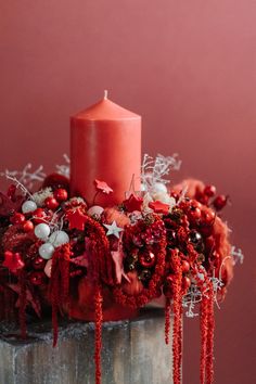 a red candle is sitting on top of a wooden stand with decorations and berries around it