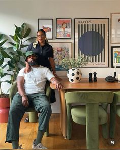 a man and woman sitting at a wooden table in front of pictures on the wall