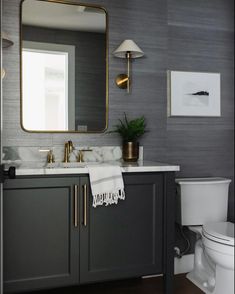 a white toilet sitting next to a sink in a bathroom under a large framed mirror