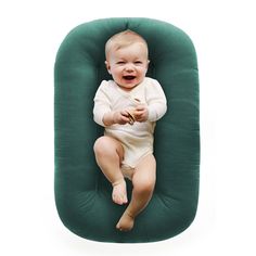 a baby is sitting on a green pillow and holding a piece of food in it's mouth