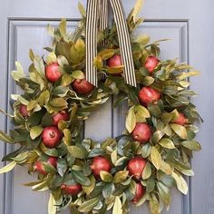 a wreath with apples and leaves hanging on a door