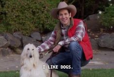 a man kneeling down next to a white dog with a cowboy hat on his head