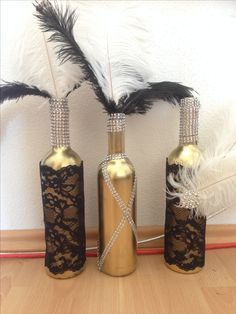 three vases with black and gold lace on them, one has feathers in it