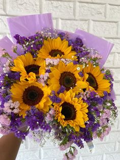 a bouquet of sunflowers and purple flowers in front of a brick wall