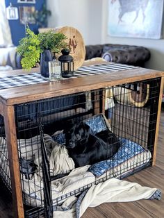 a dog laying in its cage on the floor next to a table with pillows and blankets