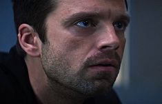 a close up of a man with blue eyes looking at something in the distance while wearing a black jacket