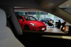 a red car parked in front of a group of people sitting at desks next to each other