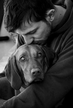 a man hugging his dog while sitting on the floor in front of a laptop computer