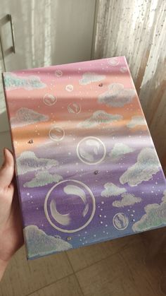 someone is holding up a box with clouds and planets painted on it in front of a window