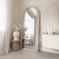 a white vase with flowers sitting on top of a table next to a large mirror