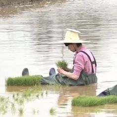 a woman sitting on the ground in water with grass growing out of her feet and wearing a hat