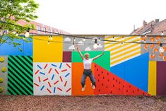 a man jumping in the air with his arms up against a colorful wall painted with different colors and shapes