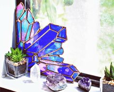 a stained glass butterfly sitting on top of a window sill next to potted plants