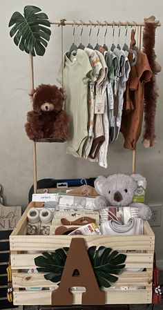 a wooden crate filled with baby clothes and teddy bears next to a wall mounted coat rack