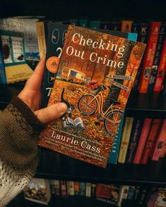 a person holding up a book in front of a bookshelf