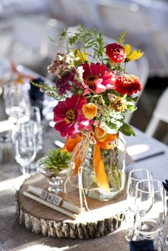 a vase filled with colorful flowers sitting on top of a wooden table next to wine glasses