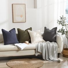 a living room filled with lots of pillows on top of a white couch next to a potted plant