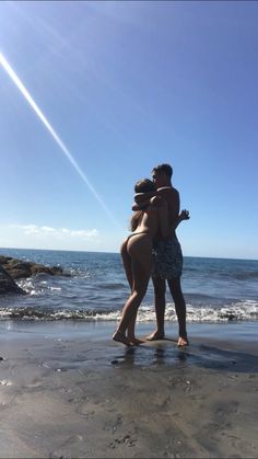 two people standing on the beach hugging each other