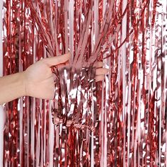 a hand reaching for some red tinsel hanging from the ceiling in front of a wall