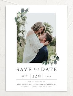 an elegant photo save the date card with greenery and flowers is shown in white