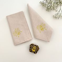 two napkins with embroidered bees on them next to a small flower and some white flowers