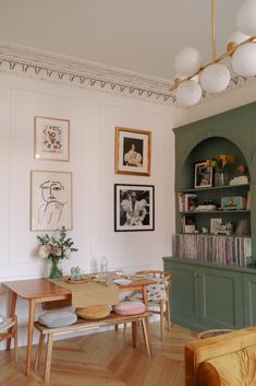 a dining room table and chairs in front of a bookcase with pictures on the wall