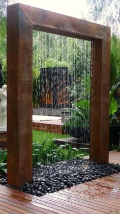 an outdoor fountain in the middle of a wooden deck with rocks and plants around it