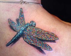 a colorful dragonfly tattoo on the back of a woman's shoulder