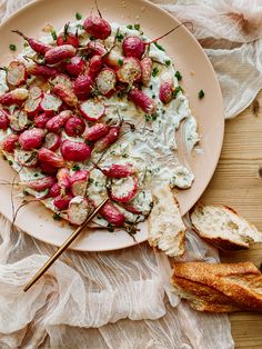 a white plate topped with sliced strawberries and cream cheese next to bread on a table