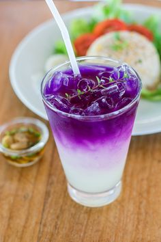 a purple drink sitting on top of a wooden table next to a plate of food