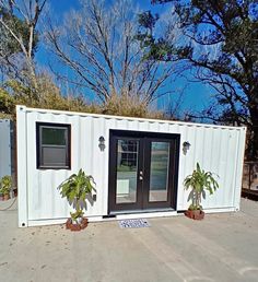 a white shipping container sitting on top of a cement ground next to trees and bushes