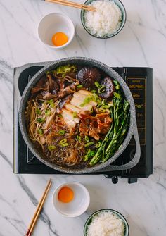 a pan filled with meat and veggies on top of a stove next to bowls of rice