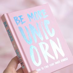 a person holding up a pink book with the words be more unic orn on it