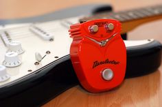 a red guitar pedal sitting on top of a wooden table next to an electric guitar