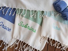 three towels with names on them sitting on a wooden floor next to a blue and white towel