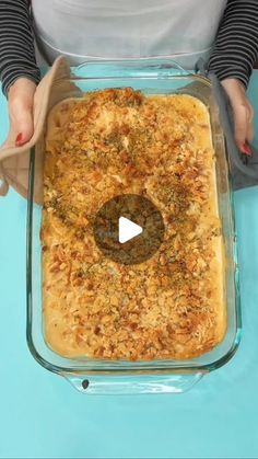 a woman is holding a casserole dish with food in it on a blue table