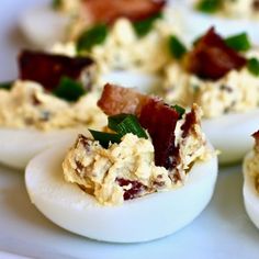 several deviled eggs with bacon and green garnish on them sitting on a white plate