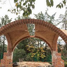 an arch in the middle of a brick wall and stone bench under it, surrounded by trees