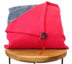 a red pillow sitting on top of a wooden table next to a pair of jeans