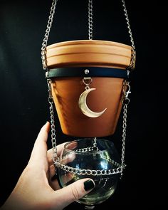 a hand holding a pot with chains hanging from it's sides and the moon on top