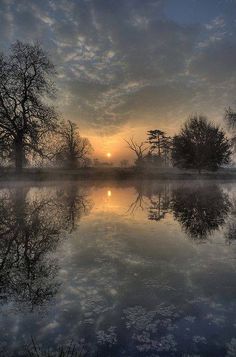 the sun is setting over a lake with trees in the foreground and clouds in the background