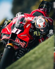 a man riding on the back of a red motorcycle down a lush green hill side