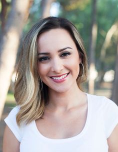 a woman with blonde hair is smiling at the camera while standing in front of trees