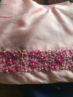 a pink dress with flowers and pearls on the side is laying on top of a bed