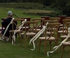 a woman sitting on top of a wooden bench next to chairs covered in white ribbon