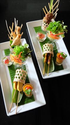 two white plates topped with food on top of green leaves covered in sauces and garnishes